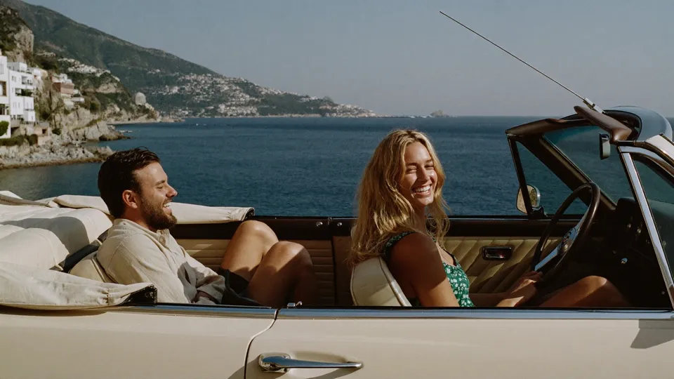 Two adult friends in a vintage convertible on the Italian coast